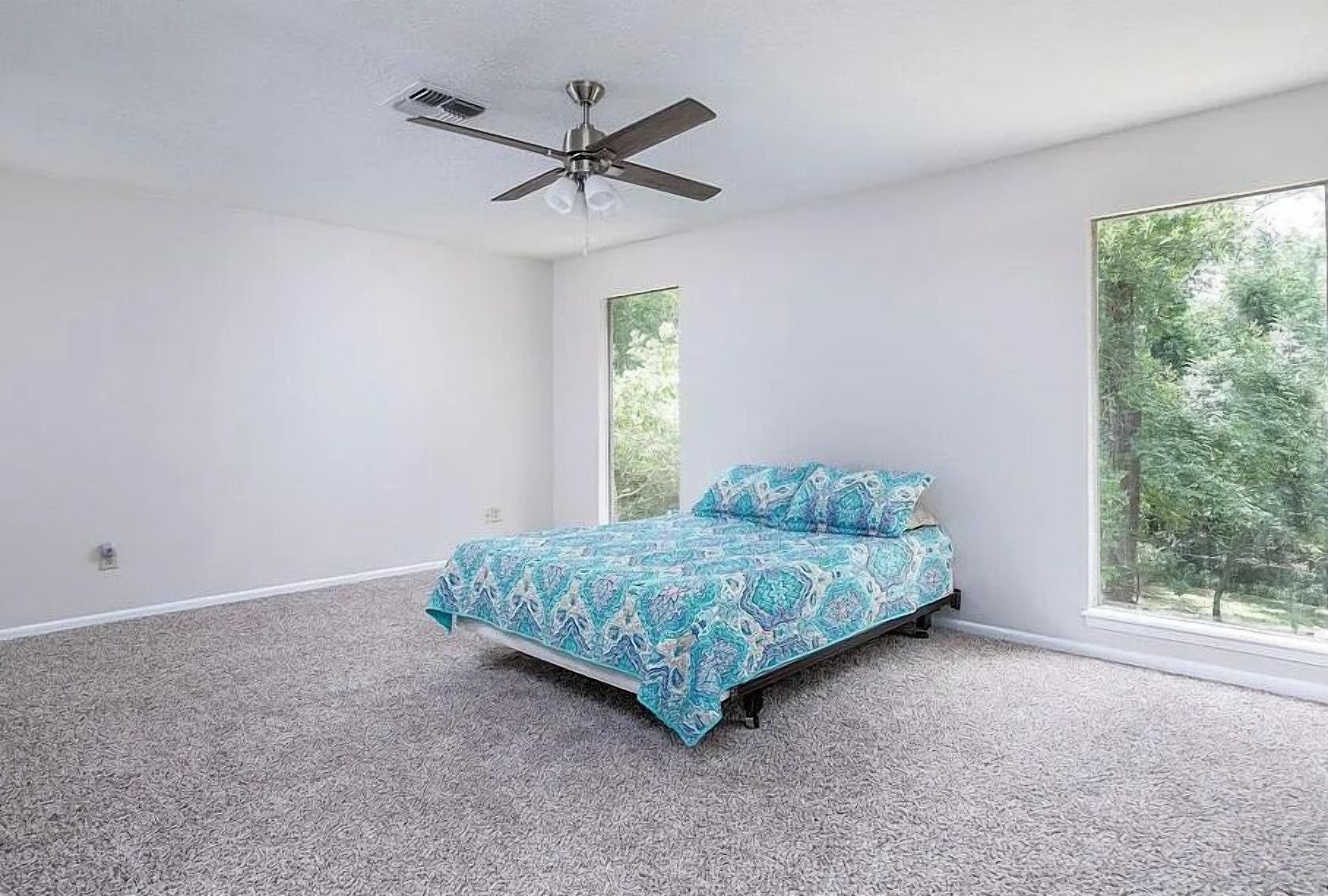 Une chambre à coucher avec un lit, un ventilateur de plafond et de grandes fenêtres.
