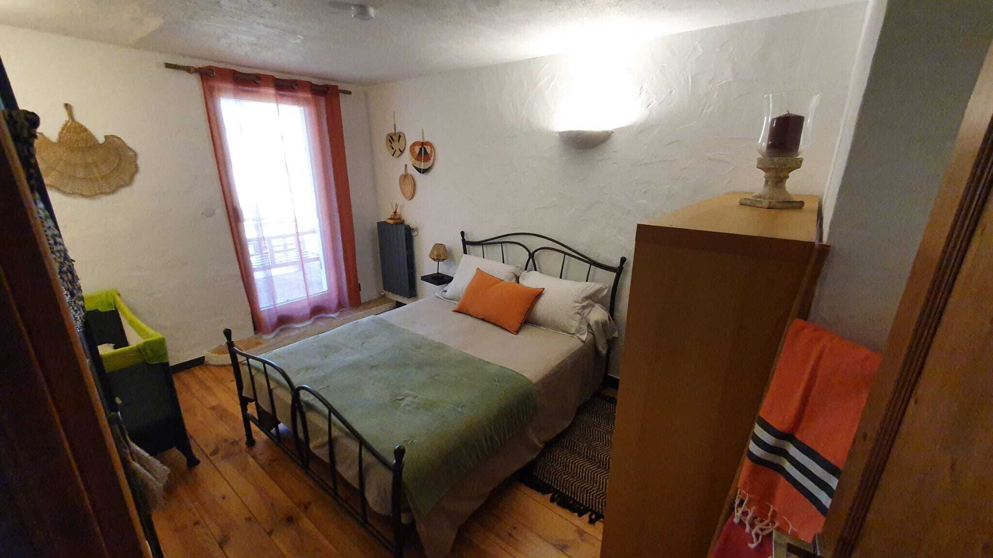 A bedroom with a bed, a nightstand, a window with curtains, a wall clock, and a small table with a candle.