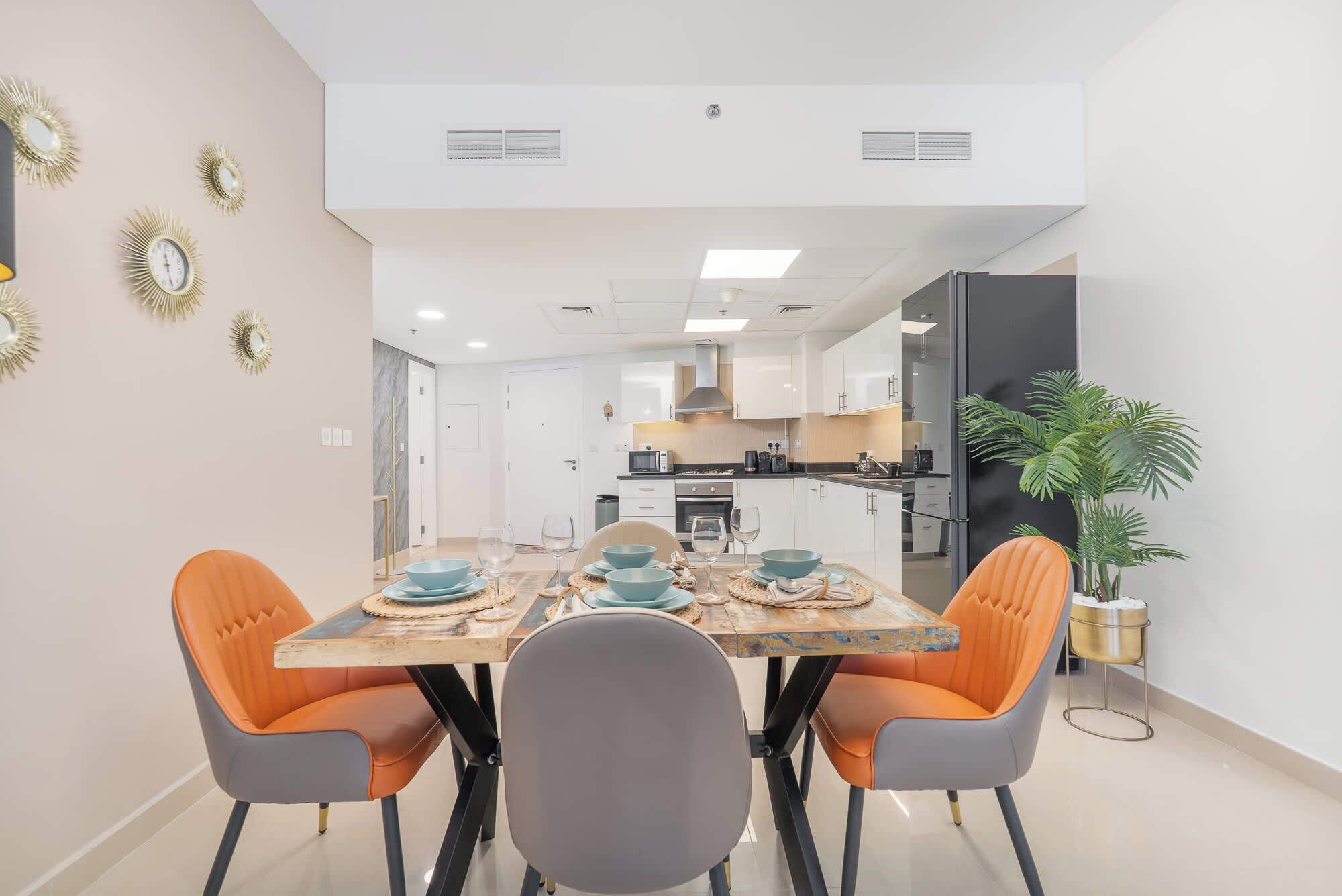A modern dining area with a wooden table, four chairs, and a kitchen in the background.
