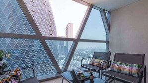 A modern balcony with a geometric glass wall, a small table with two potted plants, and a cushioned chair with a colorful cushion. - StayShort - Stylish DIFC Apartment Sleeps 4 with Pool & Gym (DIFC)