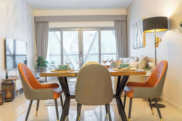 Un coin repas avec une table dressée pour quatre personnes, des chaises, une lampe sur pied et une grande fenêtre avec des rideaux.