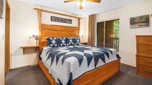 A bedroom with a wooden bed, a ceiling fan, a nightstand, and a window with curtains. - Cozy Timbers - Charming Condo for 6 with Resort-style Amenities (Branson)