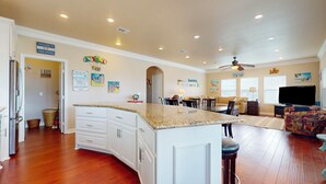 A spacious kitchen with a large island, a dining area with chairs, a sofa, and a TV. - Puddin Place: 3 BR, 2.5 BA House in Crystal Beach, Sleeps 10 (Bolivar Peninsula)