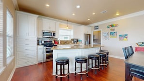 A kitchen with white cabinets, a granite countertop, stainless steel appliances, and a bar area with stools. - Puddin Place: 3 BR, 2.5 BA House in Crystal Beach, Sleeps 10 (Bolivar Peninsula)