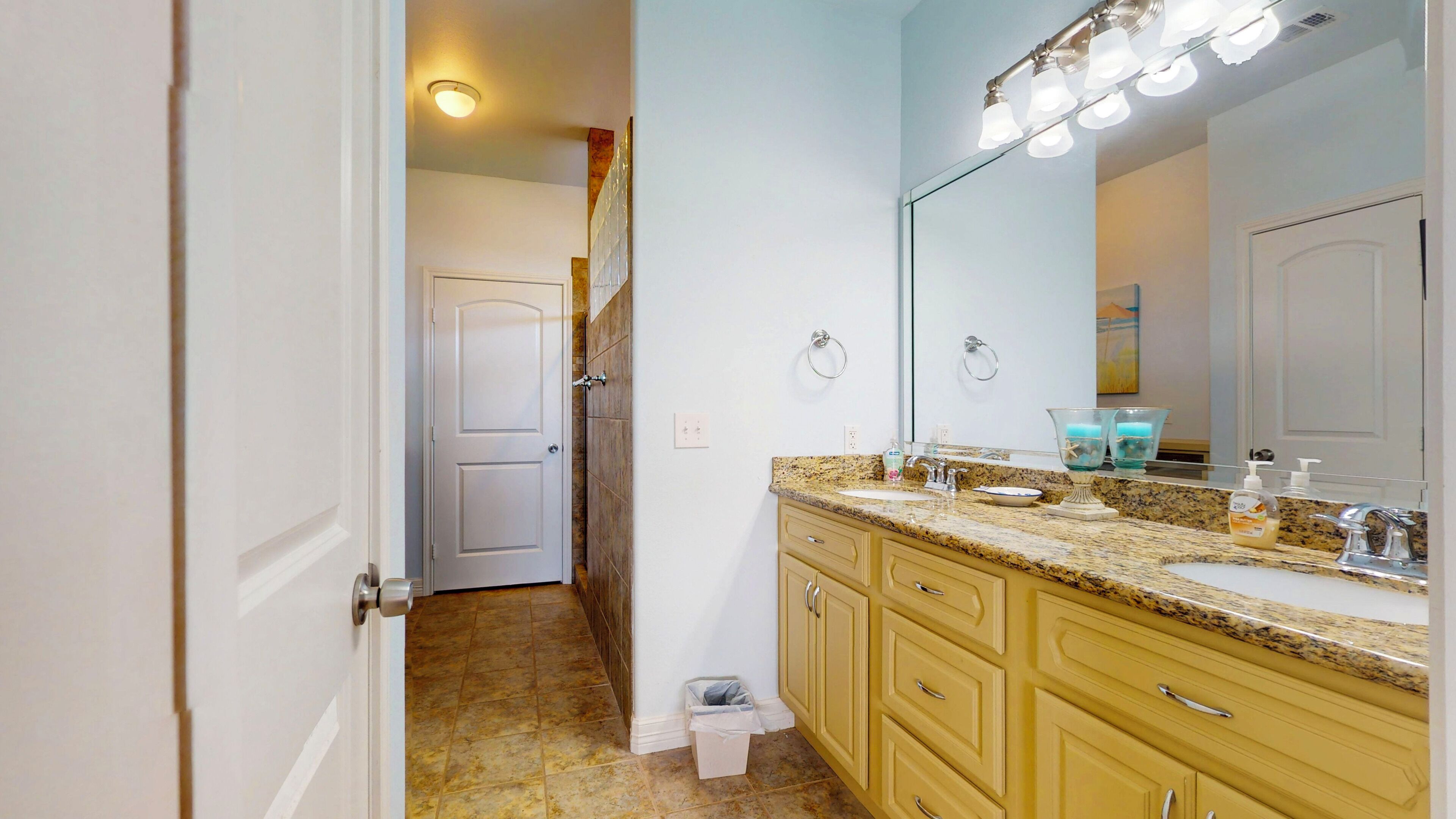 A bathroom with a granite countertop, a sink, a mirror with lights, and a towel rack.