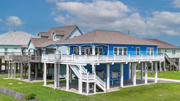 A waterfront house with a deck, stairs, and a covered area. - Puddin Place: 3 BR, 2.5 BA House in Crystal Beach, Sleeps 10 (Bolivar Peninsula)