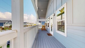 Une terrasse en bois couverte, dotée d’une rambarde, d’une chaise en bois et d’une fenêtre.