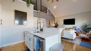 Une cuisine moderne dotée d’un îlot central, d’un coin repas avec un canapé, d’un téléviseur fixé au mur et d’un escalier menant à un niveau supérieur.