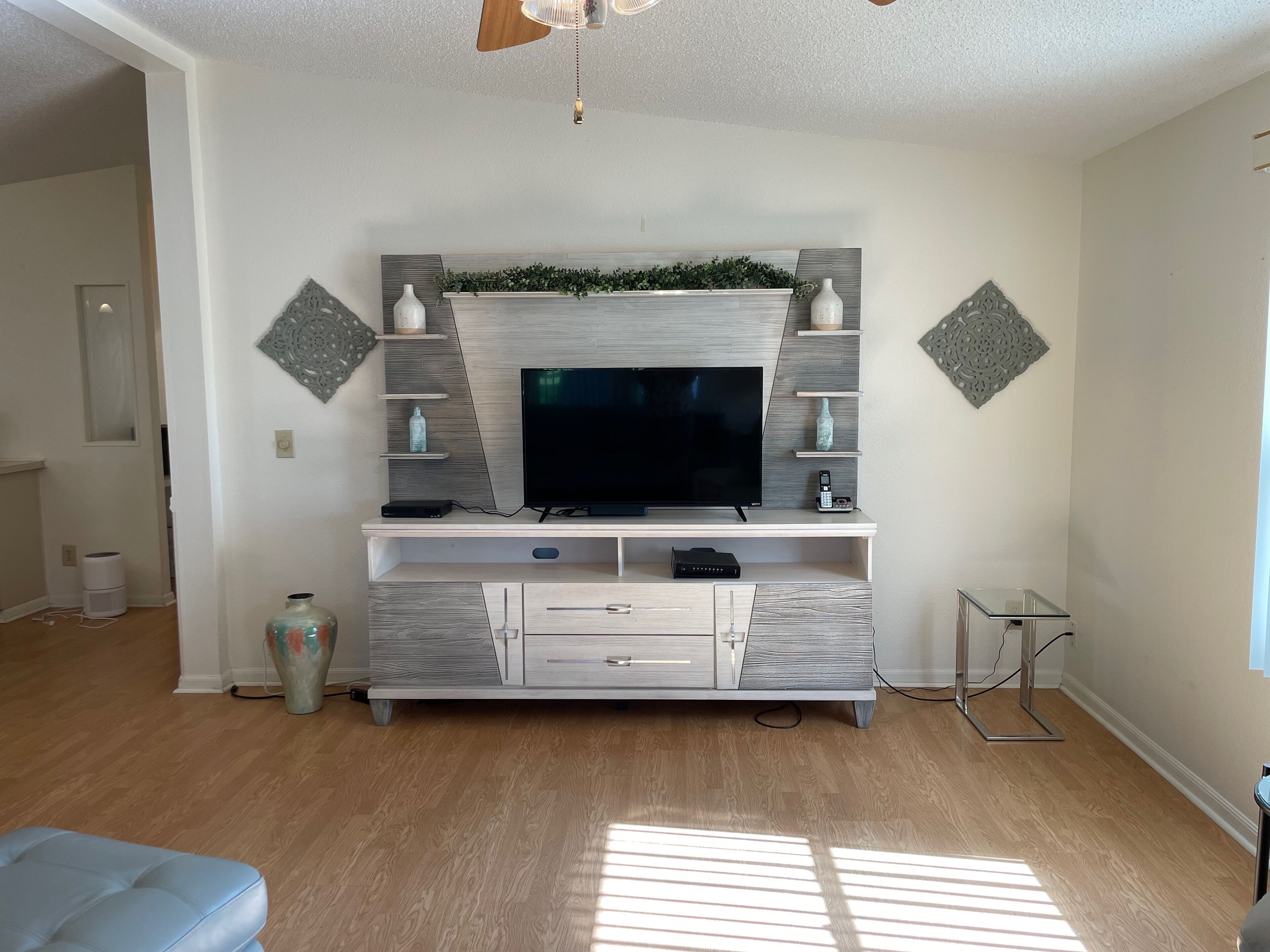 Un salon moderne doté d’un meuble de rangement intégré pour les appareils multimédias, d’un plancher en bois et d’un ventilateur de plafond.