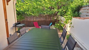 An outdoor patio with a green table and chairs, a barbecue grill, and a wooden fence.
