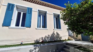 A building with three windows, each with blue shutters, and a small garden area with a statue and a fire hydrant.