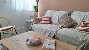 A cozy living room with a grey sofa, striped pillows, a wicker chair, and a wooden coffee table with candles and a notebook.