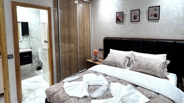 A modern bedroom with a bed, a wardrobe, and a bathroom visible through an open door.