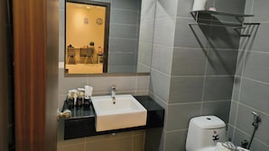 A modern bathroom with a black countertop, a white sink, and a mirror above it. There is a toilet with a "Hi" sticker on it, and a shelf with a roll of toilet paper.