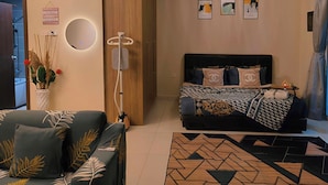 A modern living room with a sofa, a coffee table, a bed with decorative pillows, a ceiling fan, and wall-mounted artwork.