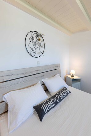 A bedroom with a wooden headboard, two white pillows, a black pillow with "HOME where your HEART" text, a wall-mounted artwork, and a bedside table with a lamp. - Paros Beach Studio Casa Costa Oro, 300m from Golden Beach (1BR 1BA) (Paros)