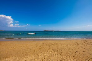 A beach with clear blue water, a boat, and a distant island. - Paros Beach Studio Casa Costa Oro, 300m from Golden Beach (1BR 1BA) (Paros)