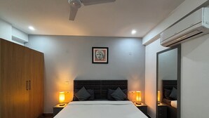 Quarto com uma cama grande, duas luminárias de cabeceira, ventilador de teto, armário, quadro na parede e aparelho de ar condicionado.