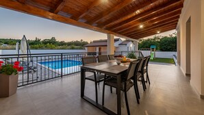 Une terrasse extérieure avec une piscine, une table à manger, des chaises et une rambarde.