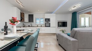 Une cuisine moderne avec des meubles blancs, une table à manger dressée avec des assiettes, des verres et une bouteille de vin. On trouve également un canapé et un téléviseur dans l’espace salon.