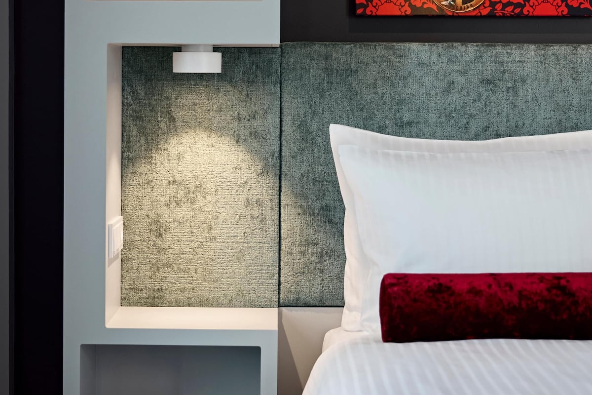 Une chambre d’hôtel moderne, dotée d’un lit, d’une tête de lit texturée et d’un luminaire fixé au mur.