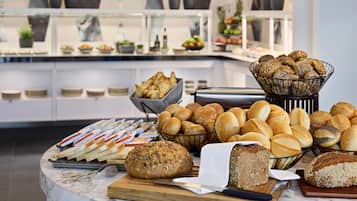 A buffet with various breads and pastries, a marble countertop, and a background with a kitchen counter and potted plants.