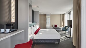 Camera d'albergo moderna con un letto, una scrivania con macchina del caffè, televisione e una poltrona.