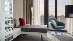 Una camera moderna con divano letto, una poltrona, una TV e un'ampia finestra con vista.
