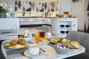 Una tavola imbandita con croissant, frutta e caffè, all'interno di una camera d'albergo moderna con vista sulla città.