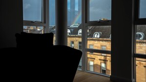 Ein Zimmer mit großen Fenstern und Blick auf eine Stadtlandschaft, mit Regenbogen und traditioneller Architektur.