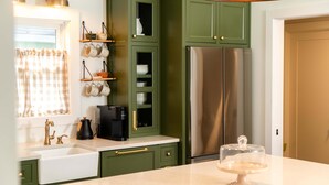 A kitchen with green cabinets, a stainless steel refrigerator, a coffee maker, and a hanging light fixture. - Magnolia Manor - Remodeled Home Near Downtown (Lake Geneva)