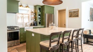 A kitchen with green cabinets, a large island, and a hanging light fixture. - Magnolia Manor - Remodeled Home Near Downtown (Lake Geneva)