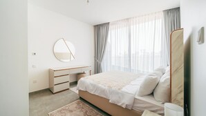 A bedroom with a bed, bedside table, mirror, and a view of the city through sheer curtains. - Cozy 1 Bedroom In High Floor In Dubai Marina (Dubai)