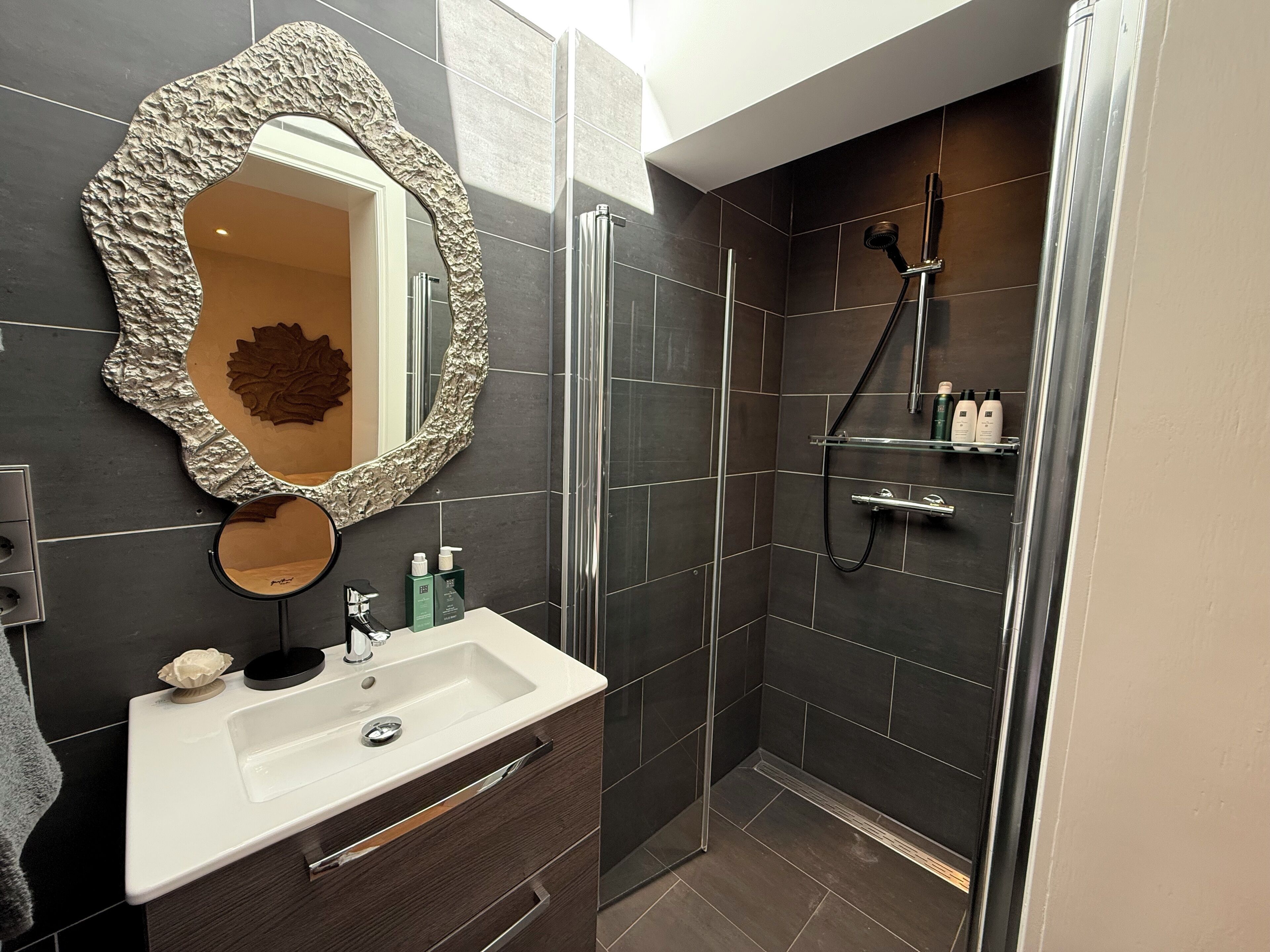 A modern bathroom with a large mirror, a sink, and a shower area.