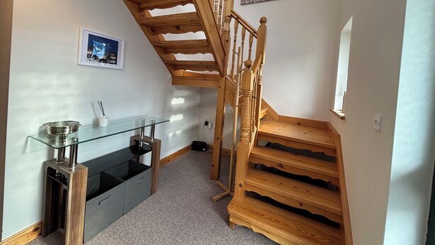 A modern kitchen with a glass-top island, wooden staircase, and a framed picture on the wall.