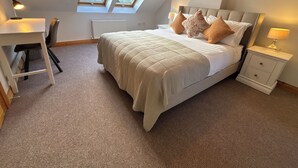 A bedroom with a bed, bedside tables, a desk, and two skylights.