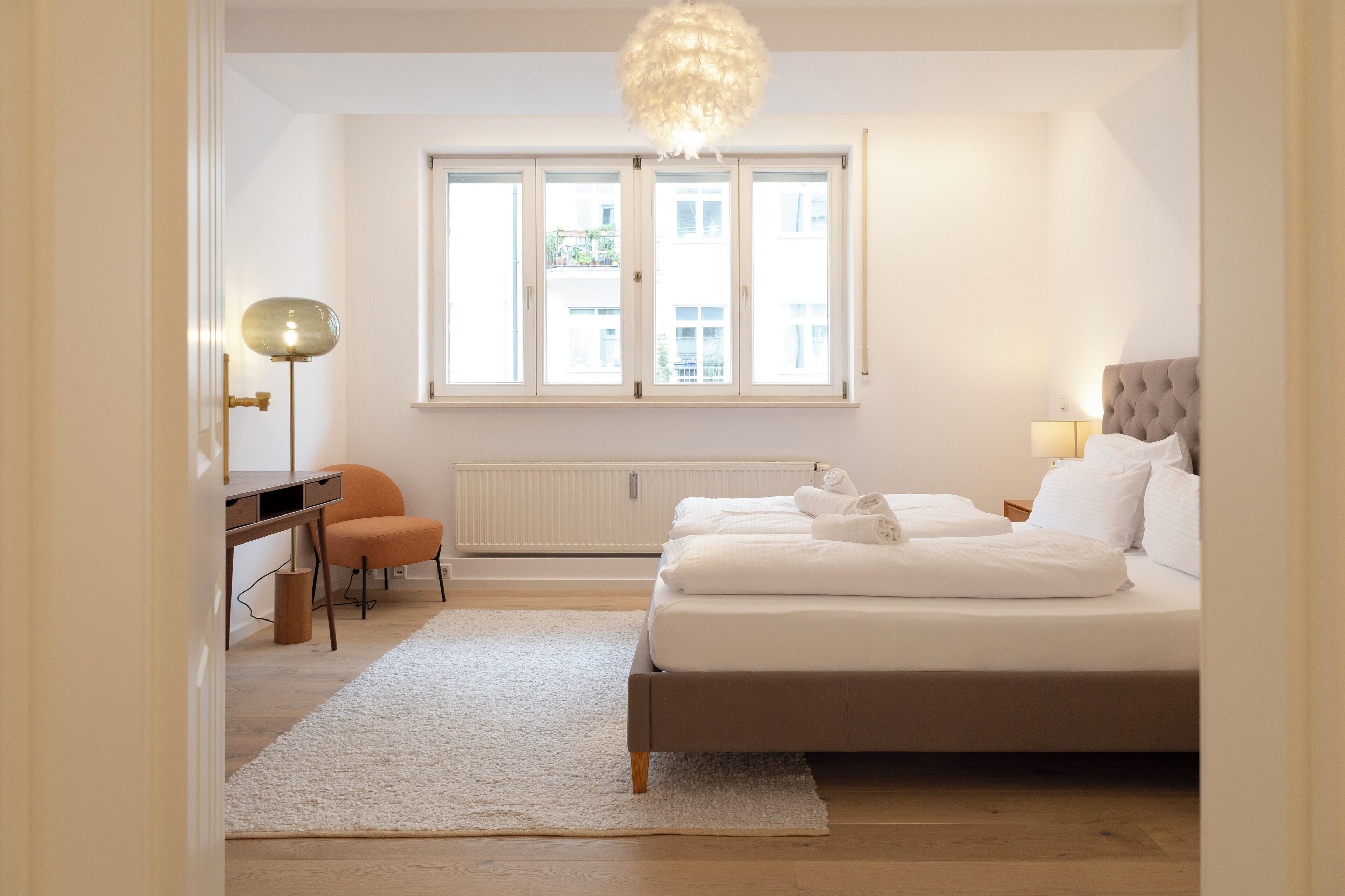 Ein Schlafzimmer mit Bett, Schreibtisch, Stuhl, Heizkörper und einem Fenster mit Blick auf Gebäude.
