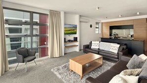 A modern living room with a sofa, coffee table, and a view of a cityscape through large windows.