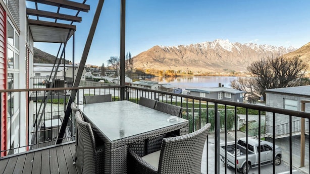A balcony with a table and chairs, overlooking a lake and mountains.
