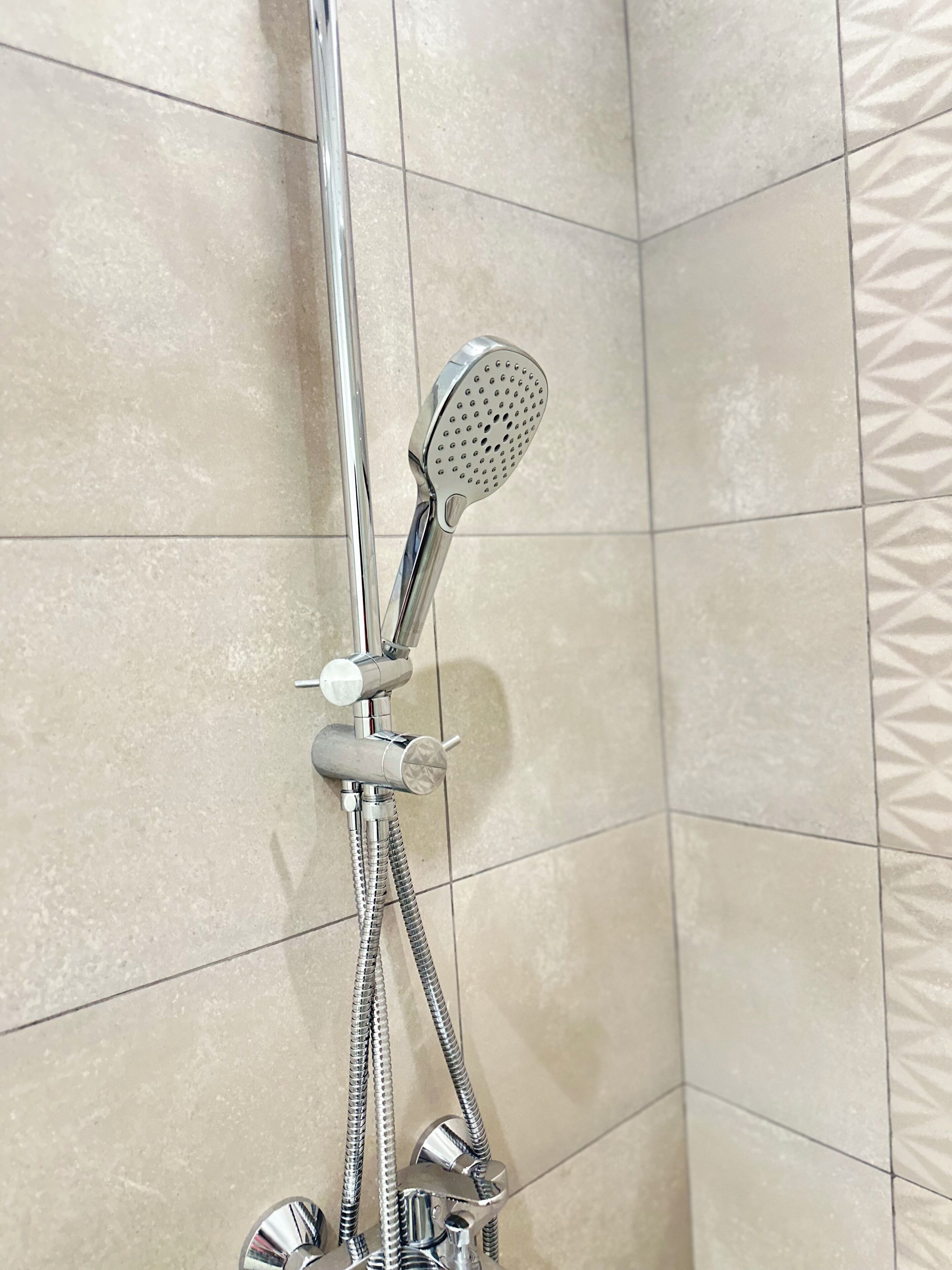 Un cabezal de ducha con un accesorio de mano, una manguera flexible y una perilla de control.