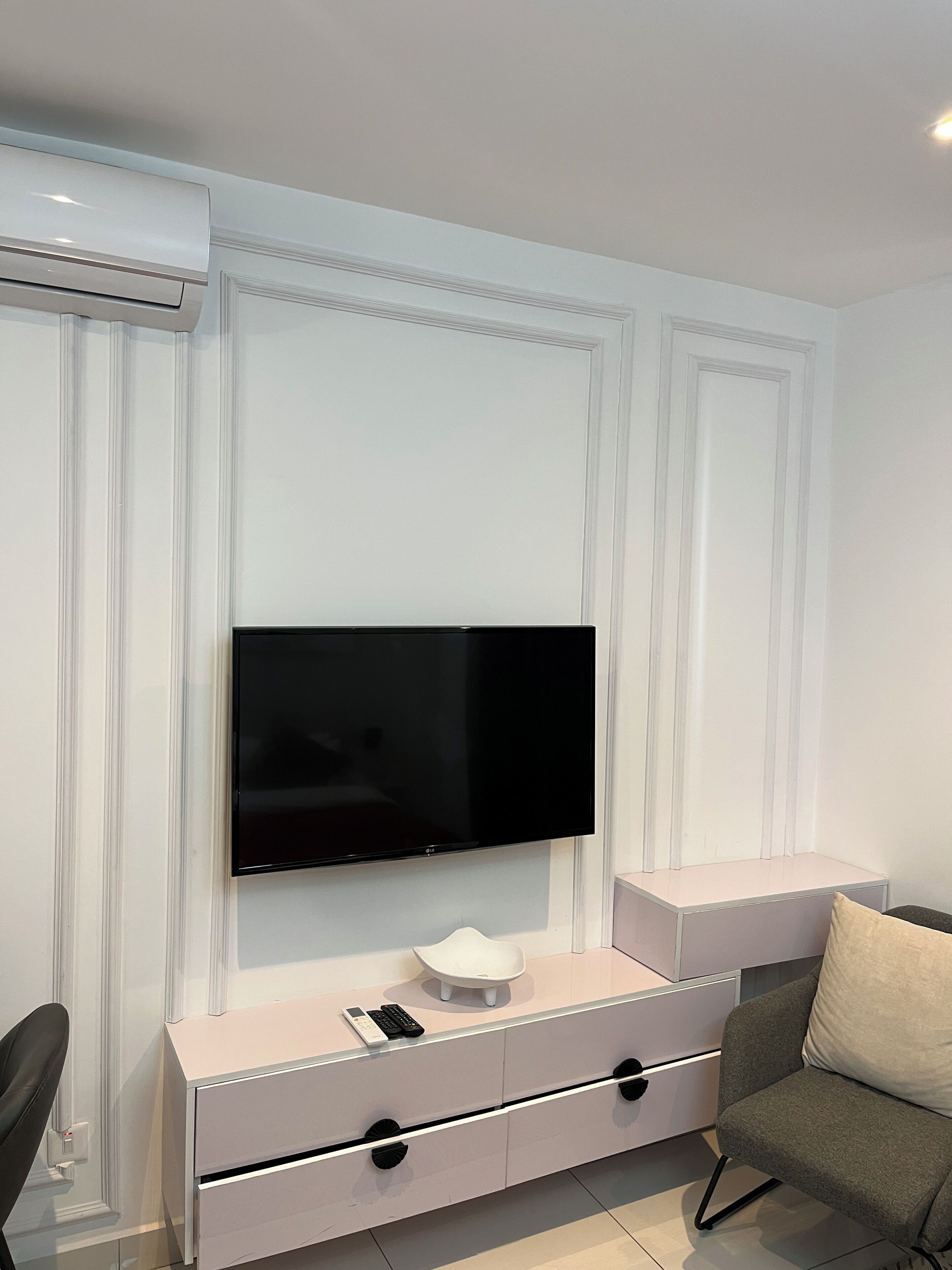 A modern living room with a flat-screen TV mounted on a white wall, a grey sofa, and a white cabinet with drawers.