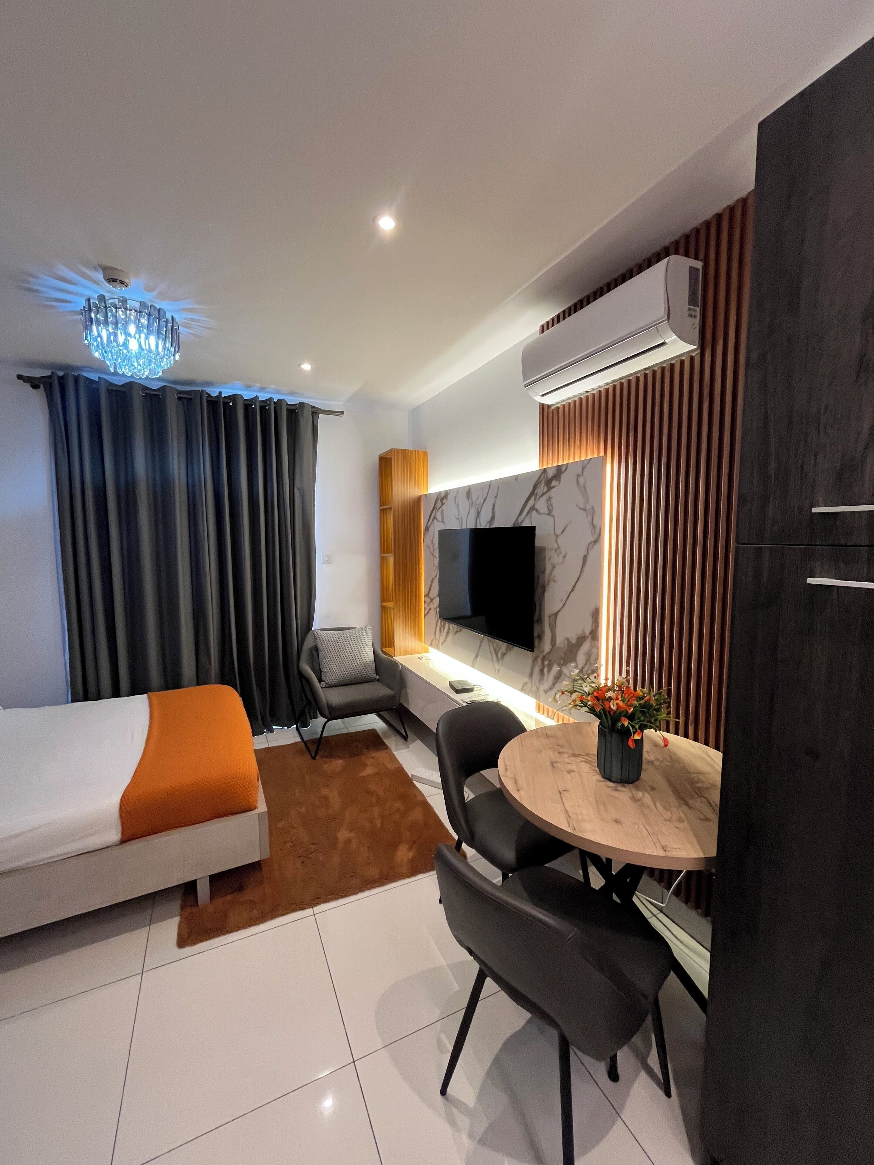A modern hotel room with a bed, a seating area with a TV, and a dining table.