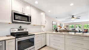 Una cucina moderna con mobili bianchi, elettrodomestici in acciaio inossidabile e un'ampia finestra che fa entrare luce naturale.