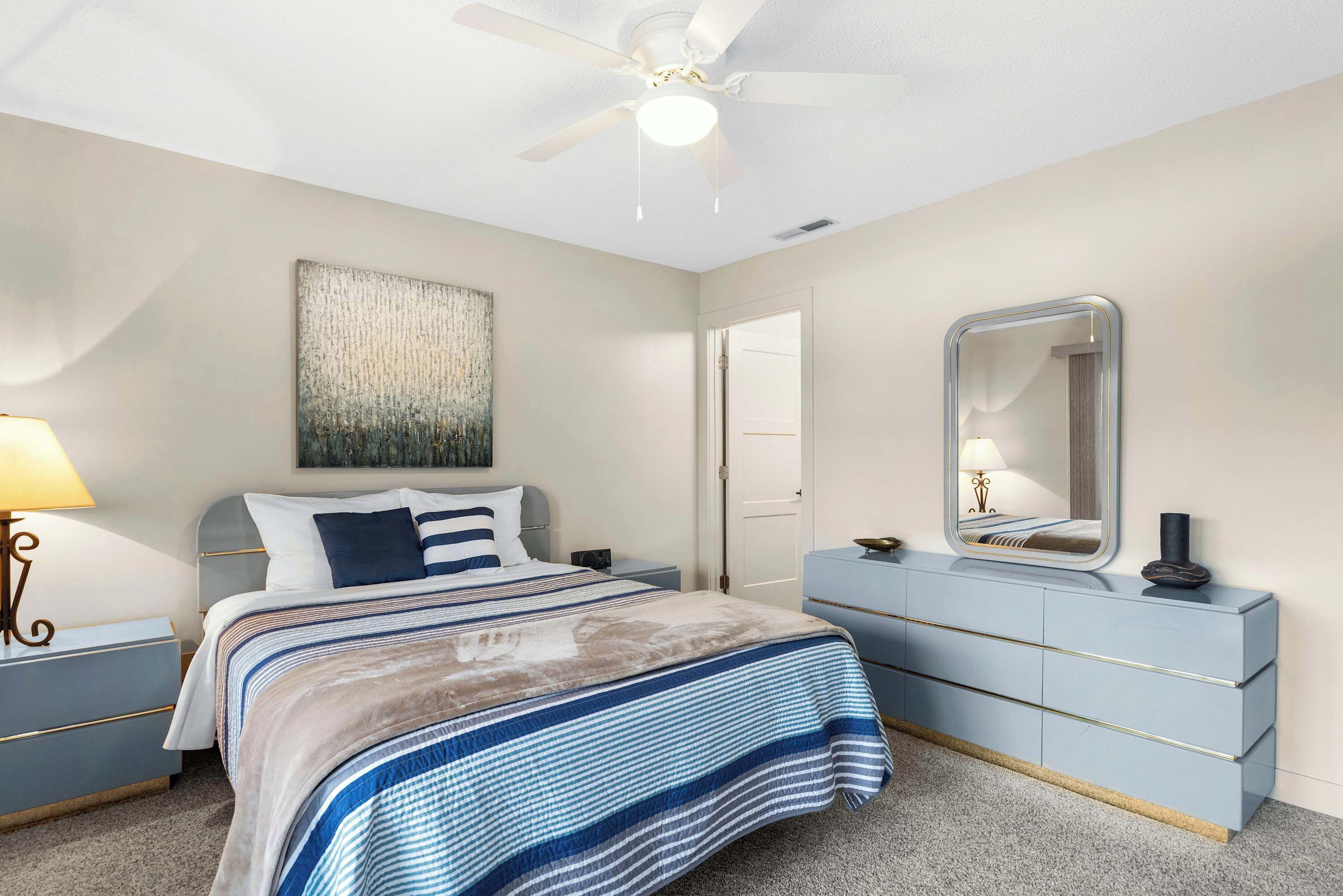 Ein Schlafzimmer mit Bett, Nachttischen, Kommode, Deckenventilator und wandmontiertem Spiegel.
