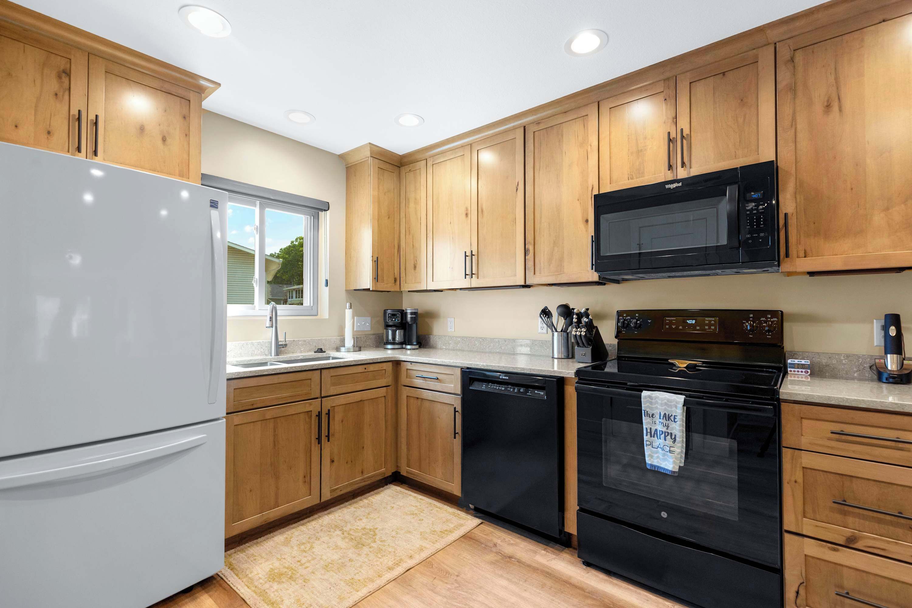 A modern kitchen with wooden cabinets, a white refrigerator, a black microwave, and a black dishwasher.