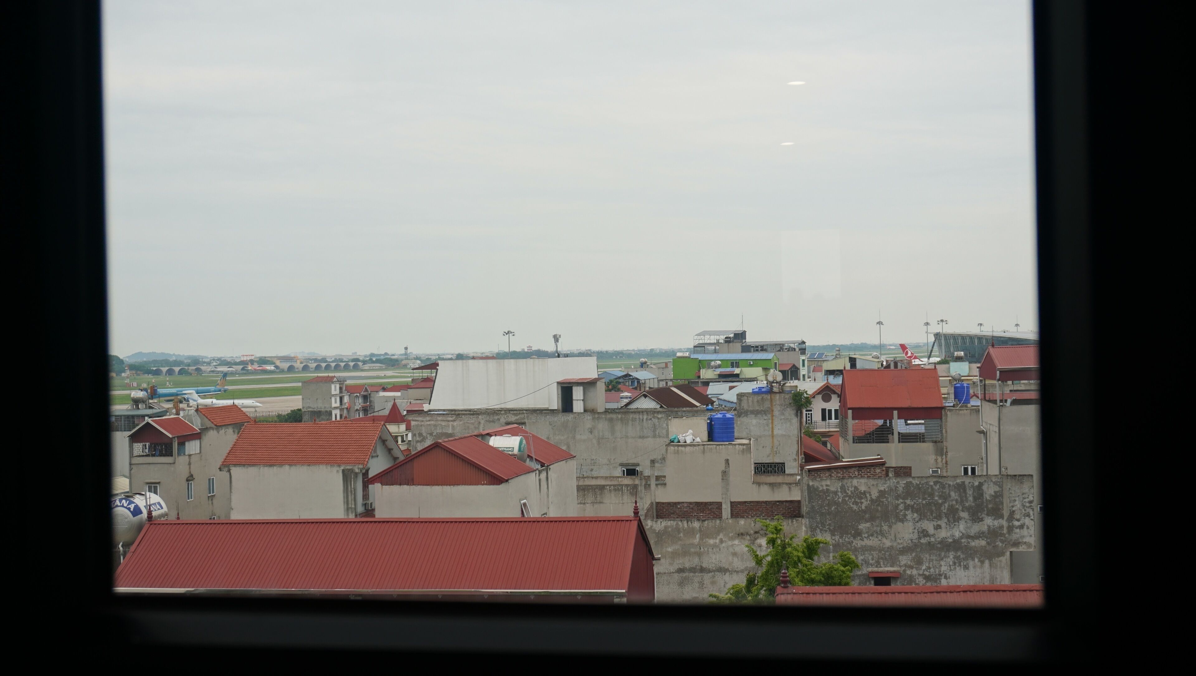 A view of a cityscape with multiple buildings, some with red roofs, and a distant airport.