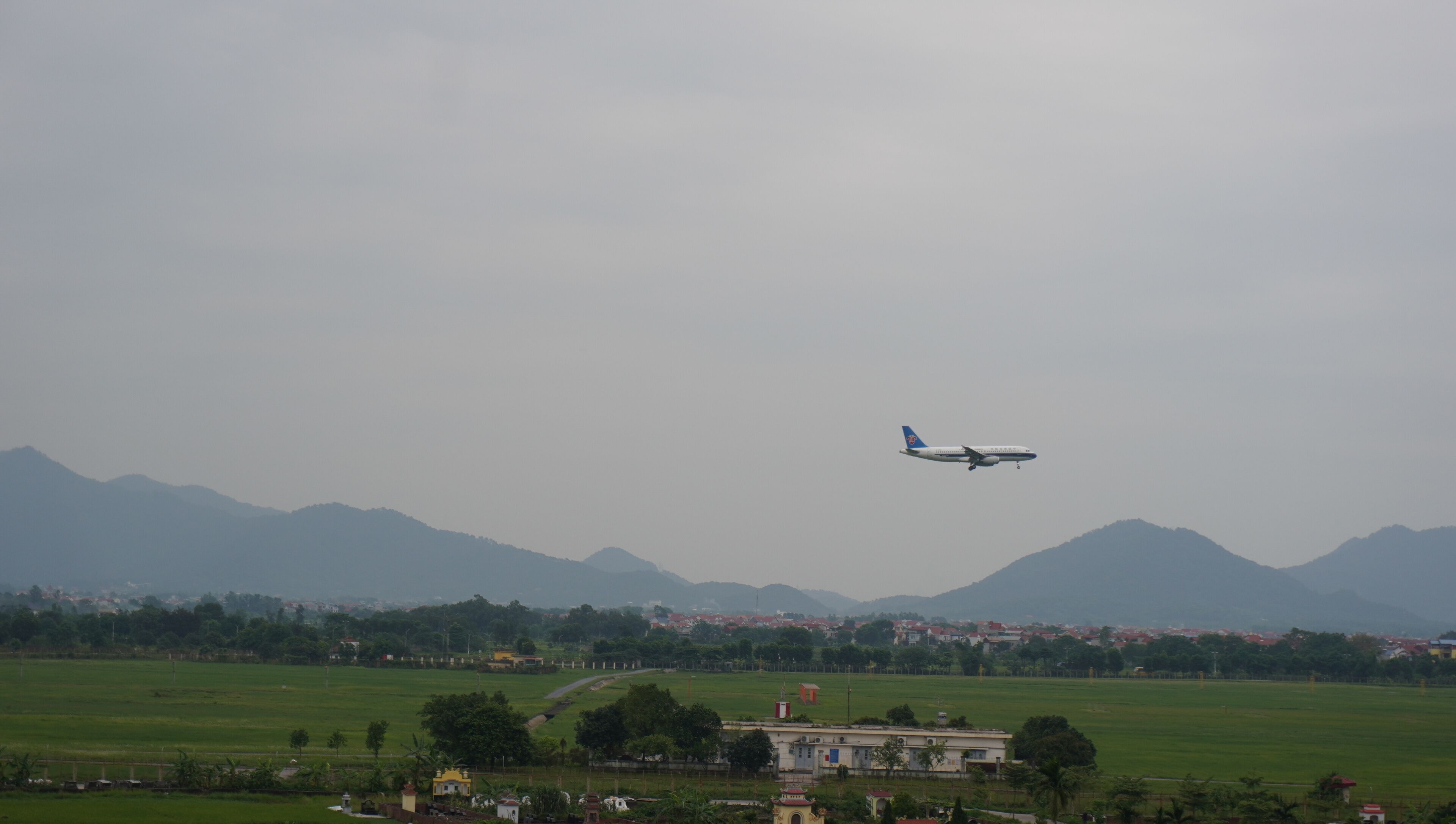 Un avion survole un paysage rural, avec des montagnes en arrière-plan.