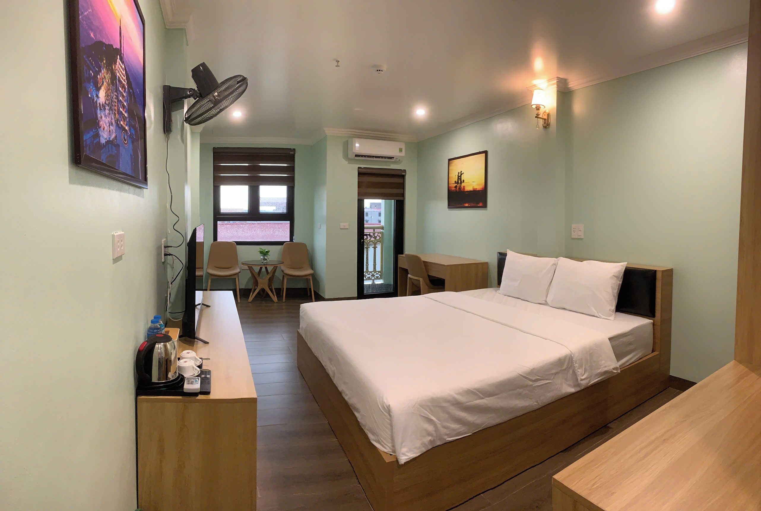 A hotel room with a bed, desk, chair, and a small table with a kettle and cups.