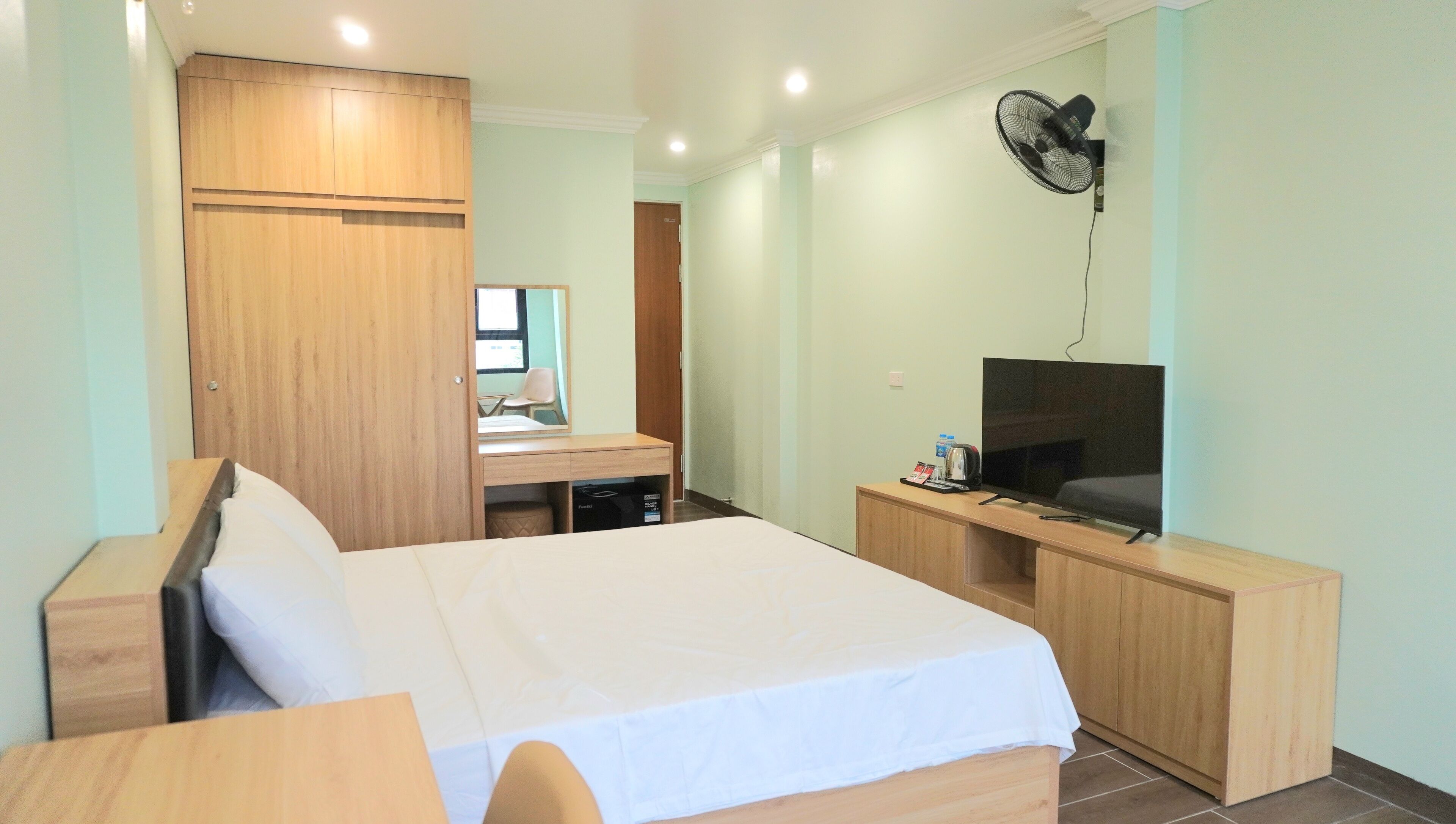 Una habitación de hotel con cama, escritorio, televisión y ventilador.