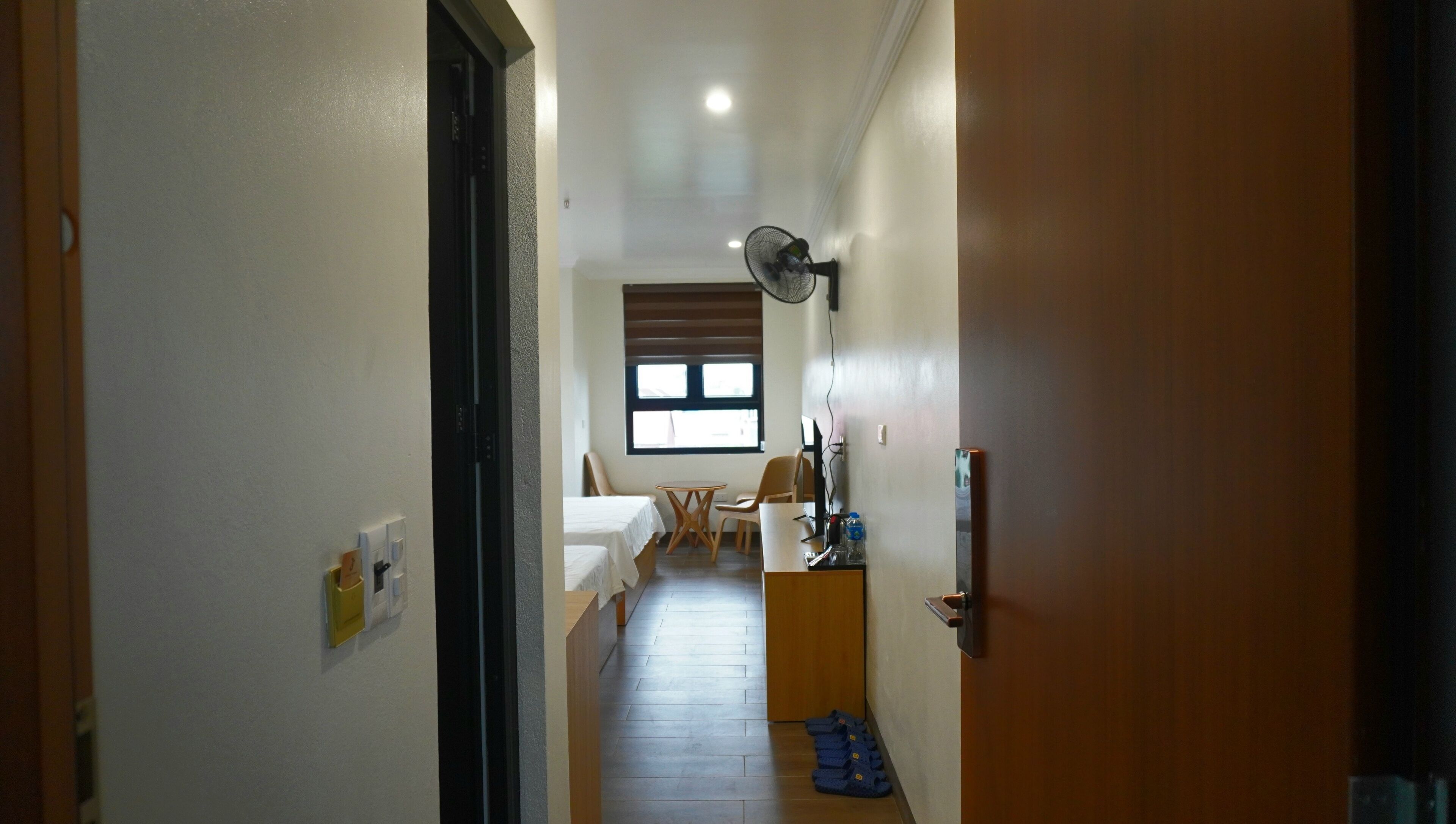 Un corridoio stretto che conduce a una camera da letto con un letto, una sedia, un tavolo e una ventola.
